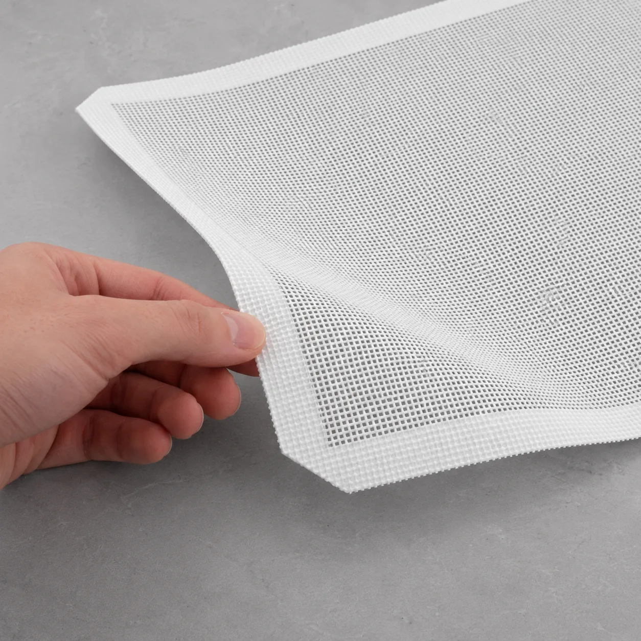Flexible edge of a silicone-coated fiberglass mesh mat being lifted by hand