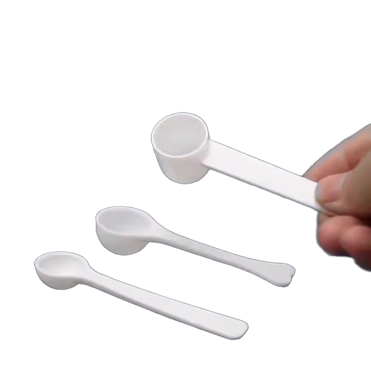 Three white plastic dosing spoons held to show relative size